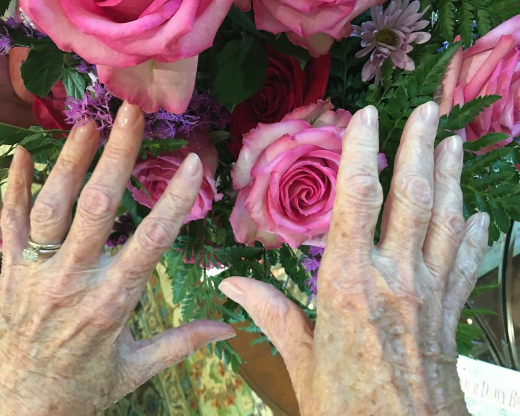 senior's hands in front of pink roses after clear manicure